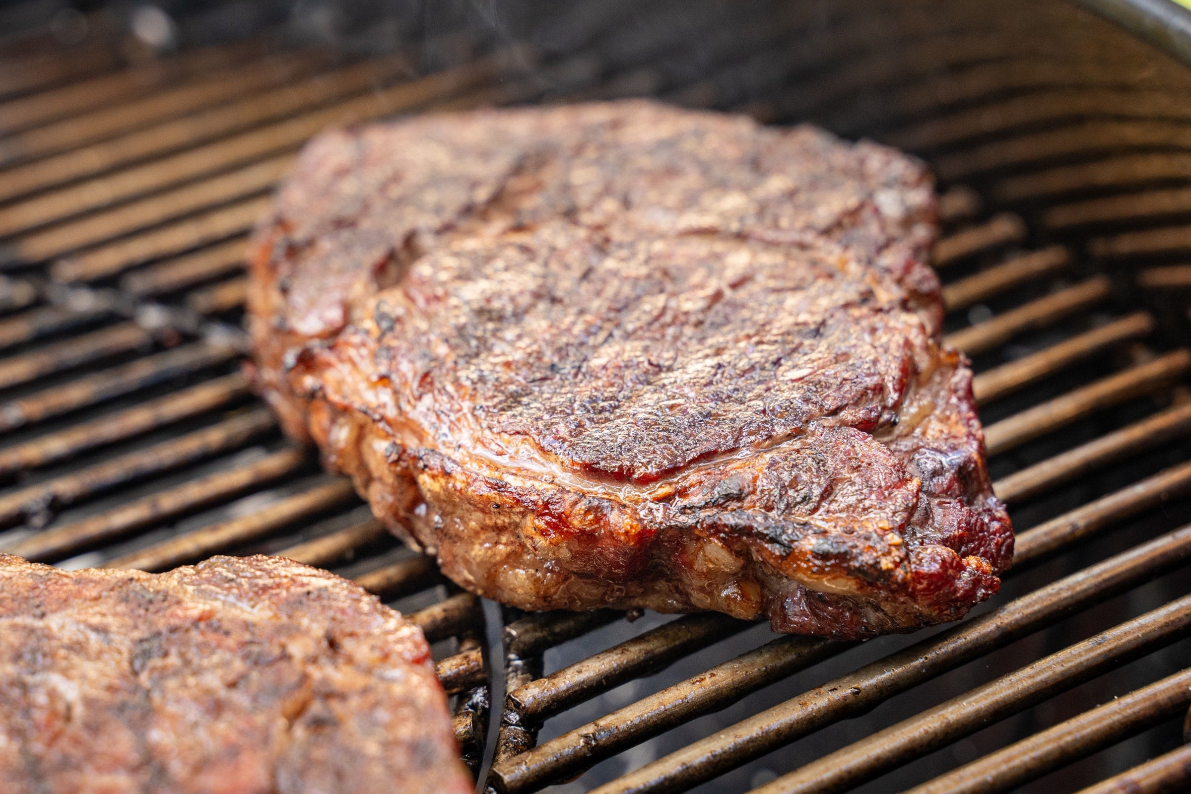 A steak being grilled on a Weber kettle grill with Woolly Bully
