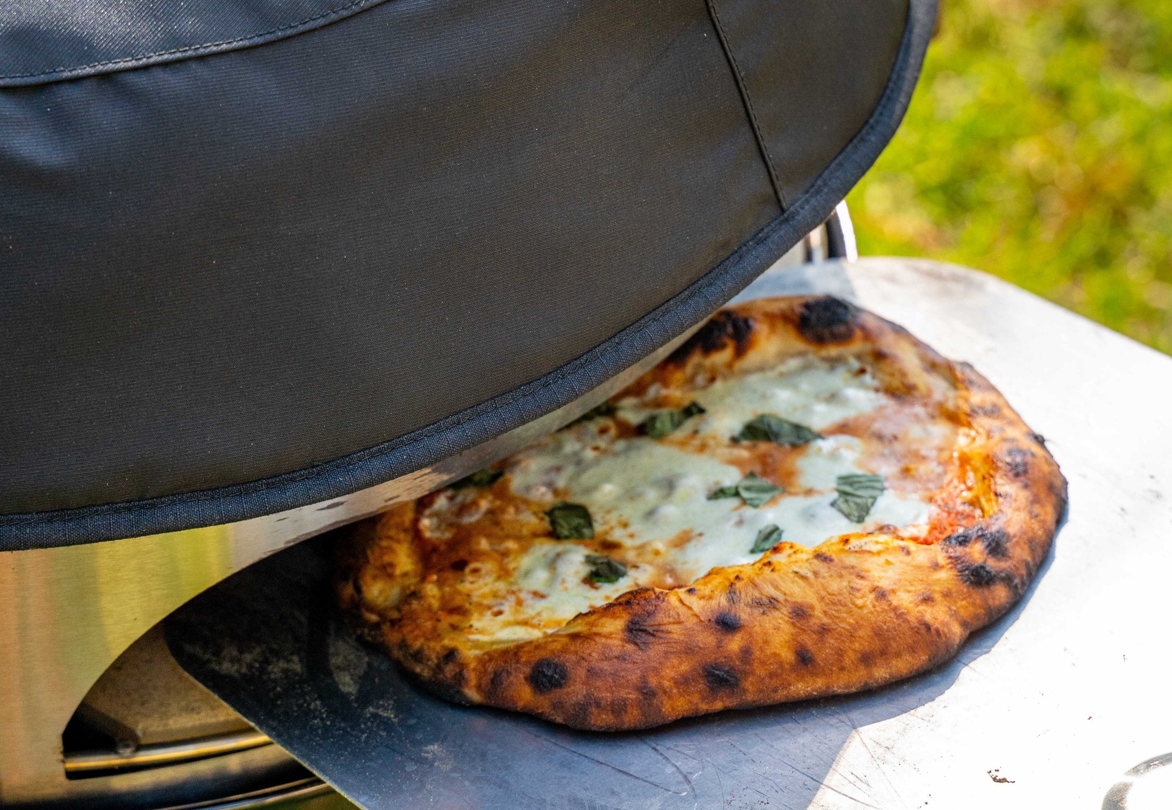 A perfectly cooked pizza being removed from a Weber kettle grill with a Woolly Bully