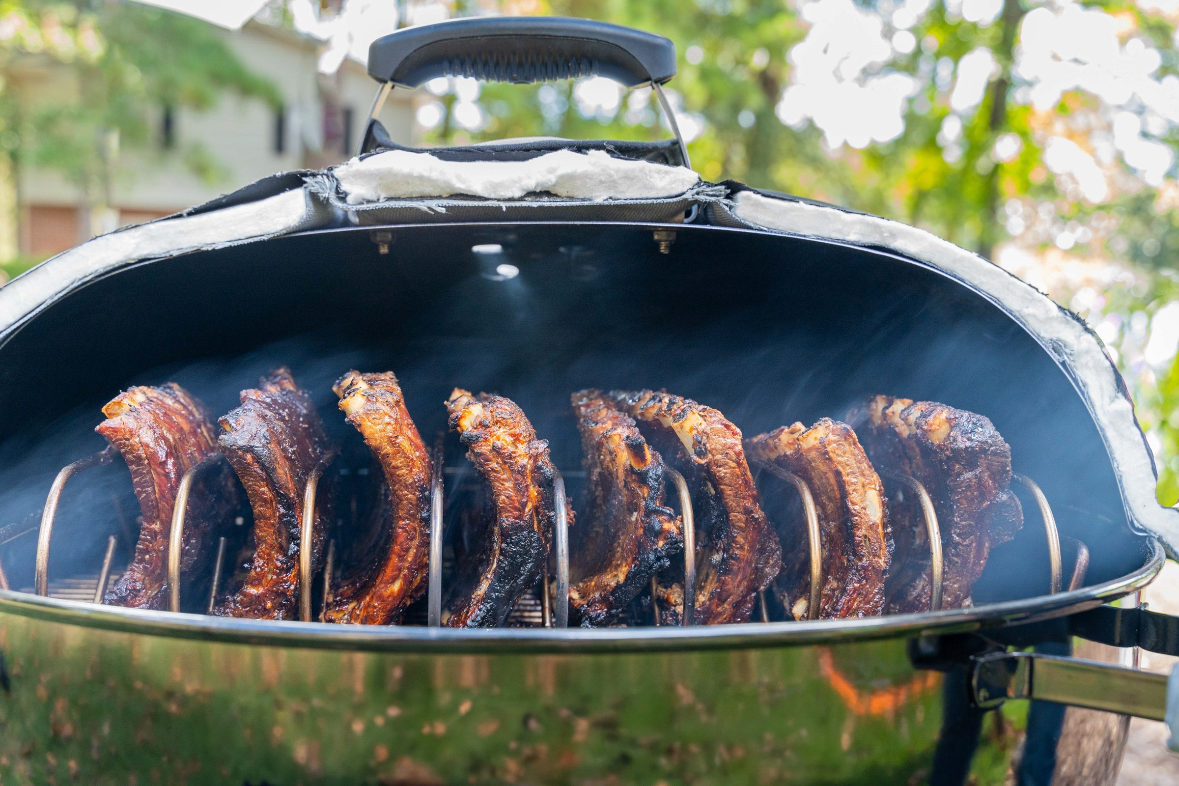 A shot of ribs cooking on a Weber kettle grill with a Woolly Bully Insulated Grill Cover.